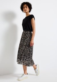 Top corto nero a maniche corte abbinato a una gonna trasparente leopardata lunghezza ginocchio. Indossato con sneakers bianche, enfatizzando un look informale.