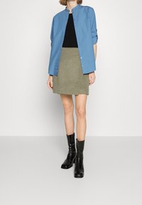 Ljust blå button-up skjorta över en svart topp, parat med en khaki mini kjol och svarta läderankelstövlar. Släta tyger med distinkta färger.