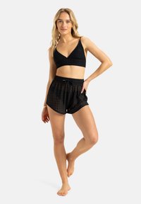 Svart bralette med et teksturert rutenettmønster, parret med svarte mesh-shorts med elastisk midje og snøring.