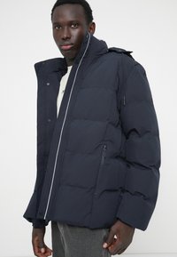 Dunkelblaues Puffer-Jacke mit einem Reißverschluss auf der Vorderseite, Druckknöpfen und einer strukturierten Kapuze. Hat ein horizontales Steppmuster und seitliche Taschen.