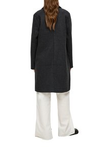 Dunkelgrauer Wollmantel mit geradem Schnitt, langen Ärmeln und minimalistischer Ausführung. Verfügt über eine Mittelnaht und wird über weißen, weiten Hosen getragen.