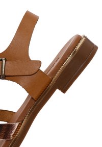 Sandalo in pelle marrone con cinghie superiori regolabili, suola piatta e accentuazione metallica lungo il bordo. Presenta una texture liscia e un design minimalista.