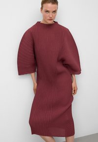 Bordeauxfarbendes, plissiertes Kleid mit hohem Kragen und übergroßen Ärmeln, aus strukturiertem Stoff und geradem Schnitt, knielanges Design.