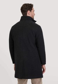 Schwarzer Wollmantel mit hohem Kragen, geradem Schnitt, mittellangem Design und sichtbaren Nahtdetails. Strukturierter Stoff.