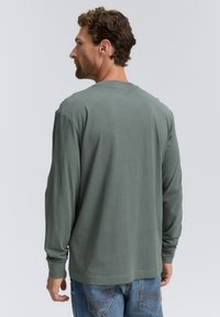 Hosszú ujjú, crewneck póló puha, olívazöld pamutból. Sima textúrájú, laza fit, látható logók vagy minták nélkül.
