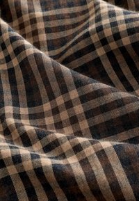 Brown and tan plaid fabric with a textured finish, featuring a repeating grid pattern of varying square sizes, creating depth and contrast.