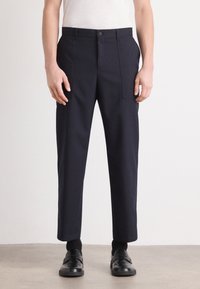 Navy trousers made of structured fabric, featuring a straight fit, side pockets, and a single button closure. Worn with black shoes.