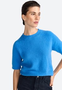 Blå kortærmet sweater lavet af blødt, tekstureret stof med en rund halsudskæring. Designet har en afslappet pasform og raglanærmer.