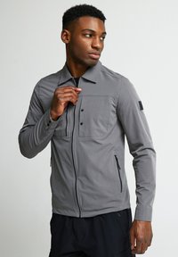 Pelēks jaku ar zipu, ar apkakles izgriezumu, divām frontālām kabatām un gludu audumu. Iespējas elegants dizains ar melniem akcentiem.