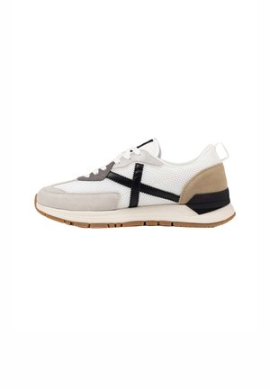 Zapatilla de running blanca con detalles en ante beige, diseño negro cruzado en el lateral, cordones blancos y suela marrón claro.