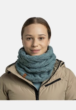 Bufanda de color azul claro de punto con un patrón de cable textura, llevada sobre una chaqueta beige con un bolsillo con cremallera y un cuello alto.