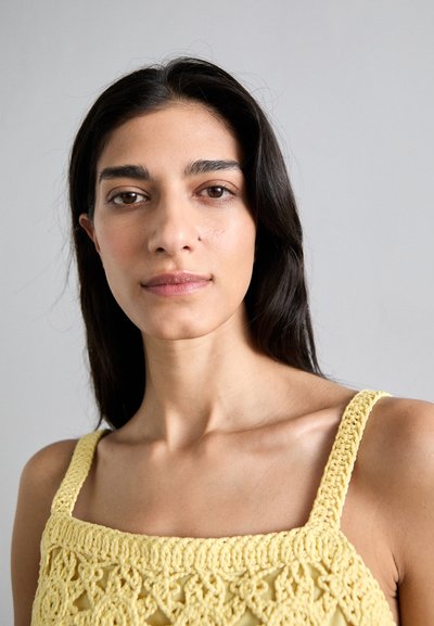 Haut au crochet jaune avec un décolleté carré et des bretelles larges, présentant des motifs complexes et un tissu doux et texturé.