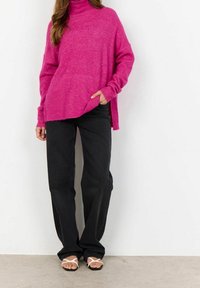 Pull à col roulé tricoté fuchsia avec une coupe décontractée, fentes sur les côtés, associé à un jean large noir et des sandales blanches. Texture lisse.