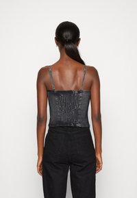 Top corsetto in denim nero con spalline sottili regolabili e pannello posteriore testurizzato. Abbinato a pantaloni neri a vita alta con tasche posteriori.