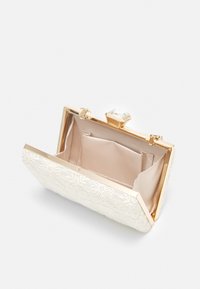 Pochette blanche brodée avec garnitures en or. Dotée d'un fermoir bijou et d'un intérieur doublé en satin avec une poche pour l'organisation.