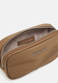 Brun stoff kosmetikkveske med sølvglidelås, beige innside og Michael Kors-logo inni. Glatt tekstur og rektangulær form.