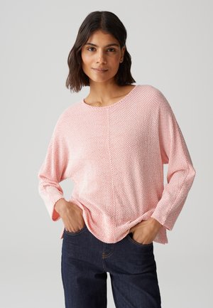 Lichtroze longsleeve top van een textuurstof, met ronde halslijn en verlaagde schouders, gecombineerd met donkerblauwe spijkerbroek.