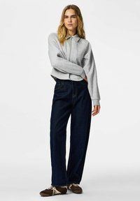 Sweat-shirt gris court avec col et fermeture éclair, associé à un jean bleu foncé ample et des baskets marron.