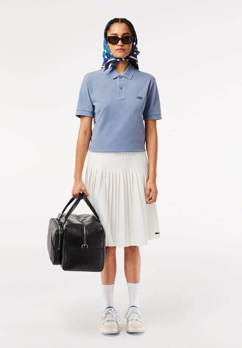 Polo de color azul claro, falda blanca con pliegues, bolso de cuero negro, gafas de sol y una bufanda estampada. Zapatillas con calcetines blancos completan el look.