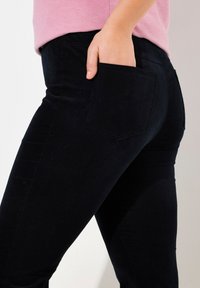 Svarta jeans med en åtsittande design, som har en bakficka och en mjuk textur. Midjan är delvis täckt av en rosa topp.