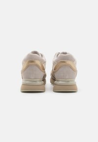 Zapatillas beige que combinan materiales de ante y malla, con puntera redonda, cuello acolchado y detalle de marca en el talón. Suela plana de goma.