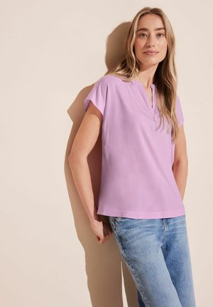 Korte mouwen, lavendelblouse met een polo-nek, gemaakt van lichtgewicht stof, gecombineerd met lichtblauwe spijkerbroeken. Eenvoudige, ontspannen pasvorm.