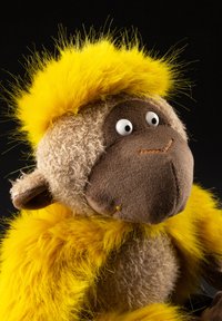 Plush monkey toy with bright yellow furry hair and body, beige textured face and ears, and large white eyes against a black background.