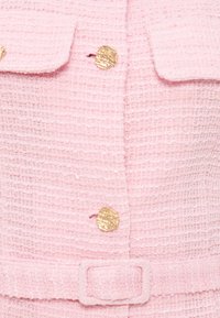 Ροζ παλτό από υφασμάτινη με υφή με χρυσά στρογγυλά κουμπιά και ζώνη από το ίδιο ροζ ύφασμα με αγκράφα.