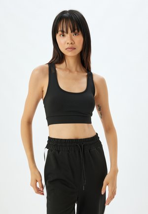 Sujetador deportivo negro con un diseño elegante, que cuenta con tirantes anchos, un escote redondeado y una textura suave. Combinado con pantalones de chándal negros sueltos.
