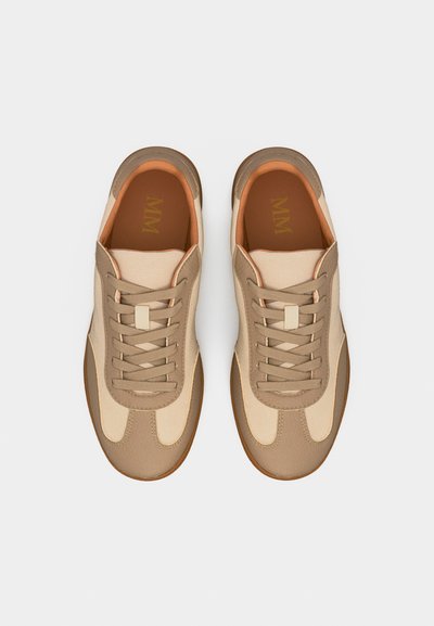 Ζευγάρι μπεζ και ανοιχτό καφέ αθλητικά παπούτσια με κορδόνια και σόλες από καουτσούκ, φωτογραφημένα από πάνω πάνω σε απλό ανοιχτό γκρι φόντο.