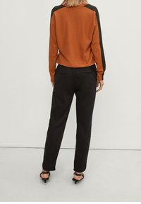 Suéter naranja con acentos negros en los hombros, combinado con pantalones negros ajustados. Texturas suaves y detalles de diseño minimalistas.