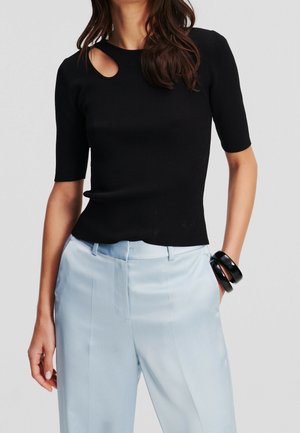 Top nero a coste con maniche corte e dettaglio a chiave sul collo, abbinato a pantaloni in satin blu chiaro e bracciali rigidi neri.