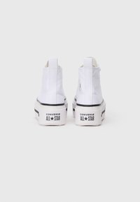 Sneakers alte in tela bianca con accenti neri in gomma, dotate di un logo sul lato e suola testurizzata, progettate per un uso casual.