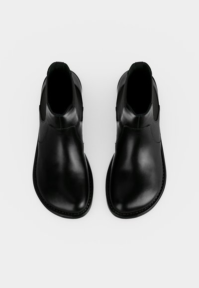 Paire de bottines en cuir noir avec bouts arrondis et panneaux latéraux élastiques, vues de dessus sur fond blanc.
