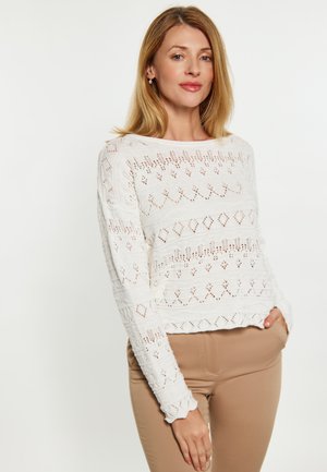 Maglione bianco lavorato a maglia con modelli testurizzati e accenti a traforo. Presenta maniche lunghe e una vestibilità comoda. Abbinato a pantaloni beige chiaro.