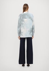 Maglietta a maniche lunghe in un delicato motivo tie-dye blu chiaro, abbinata a pantaloni larghi navy con fessure laterali.