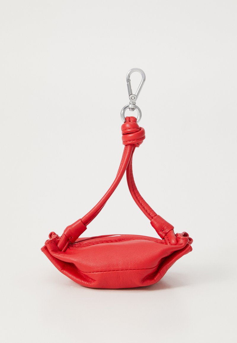 Sac à main en cuir rouge avec une anse nouée et un mousqueton en métal argenté. Forme douce et arrondie avec un design plié et une texture lisse.