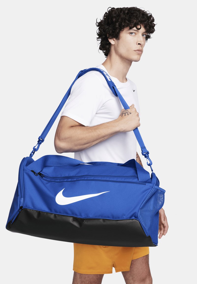 Nike sporttas in helderblauw met een zwarte onderkant, voorzien van een wit logo, verstelbare schouderriem en een gestructureerde stof.