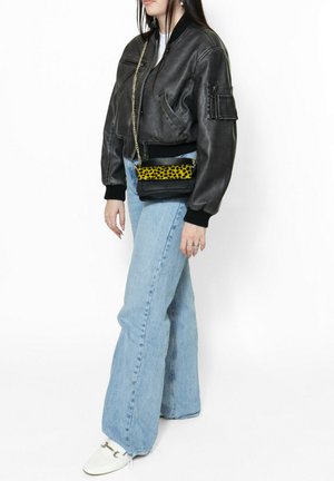 Zwarte leren bomberjack met zwarte geribbelde manchetten, lichtblauwe flare jeans en een zwarte crossbody tas met een geel luipaardprint.