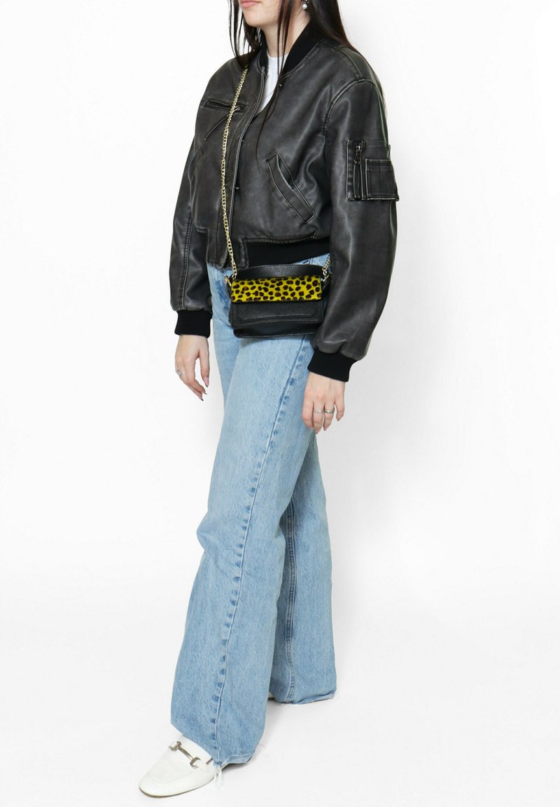 Giacca bomber nera in pelle con polsini a costine neri, jeans svasati blu chiaro e una borsa a tracolla nera con stampa leopardata gialla.