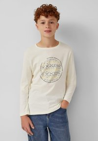 Beige langslijvende T-shirt met een ronde hals, featuring een opvallende, kleurrijke "SOUND" afbeelding op de voorkant. Gedragen met een blauwe denim jeans.