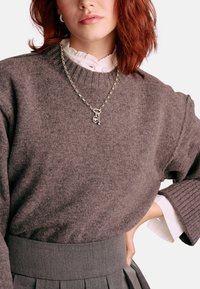 Brauner Strickpullover mit gerippten Bündchen, getragen �über einer weißen Bluse. Silberne Kettenhalskette mit Anhänger. Grauer Rock mit hohem Bund.