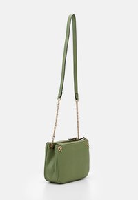 Borsa a tracolla verde con texture, chiusura a zip, dettagli in hardware dorato e tracolla a catena removibile. Design compatto e rettangolare.
