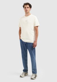Crème korte mouwen t-shirt met een ronde halslijn en vooraan bedrukte tekst. Draagt het met blauwe rechtgesneden jeans en metallic sneakers.