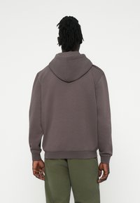 Hanorac cu glugă din bumbac gri închis cu amestec de materiale, cu manșete și tiv din tricot. Textură netedă, croi lejer și o glugă spațioasă. Design simplu.