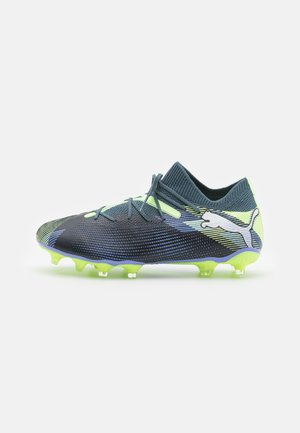 Football boots with a streamlined design, featuring a gradient blue and black upper, green accents, and a textured sole with six studs.