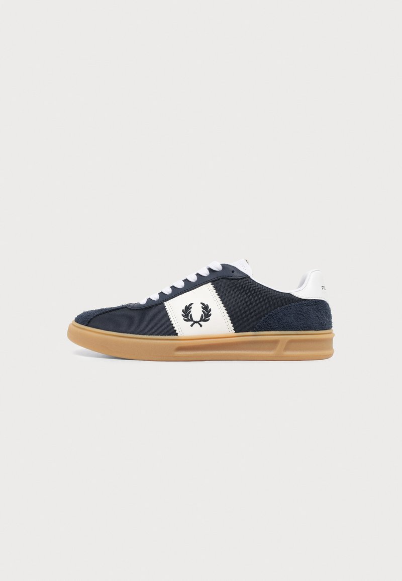 Baskets basses bleu foncé avec lacets blancs et panneau latéral arborant un logo couronne de laurier noir, et une semelle en caoutchouc marron clair.