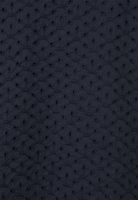 Tissu marine brodé présentant un motif ajouré texturé avec de petites ouvertures, créant une apparence délicate mais structurée.