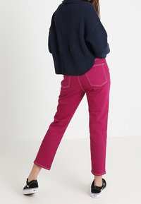 Gekürzter marineblauer Pullover mit Strickstruktur, kombiniert mit hoch taillierten rosa Hosen mit weißen Nähten und schmalem Bein, getragen mit schwarzen Schuhen.