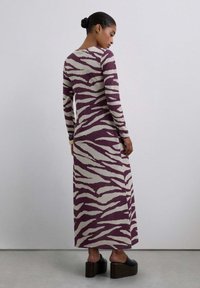 Vestido maxi de manga larga en crema con rayas de cebra burdeos; tejido de punto suave, ajustado en la parte superior, silueta fluida, combinado con zapatos de plataforma.